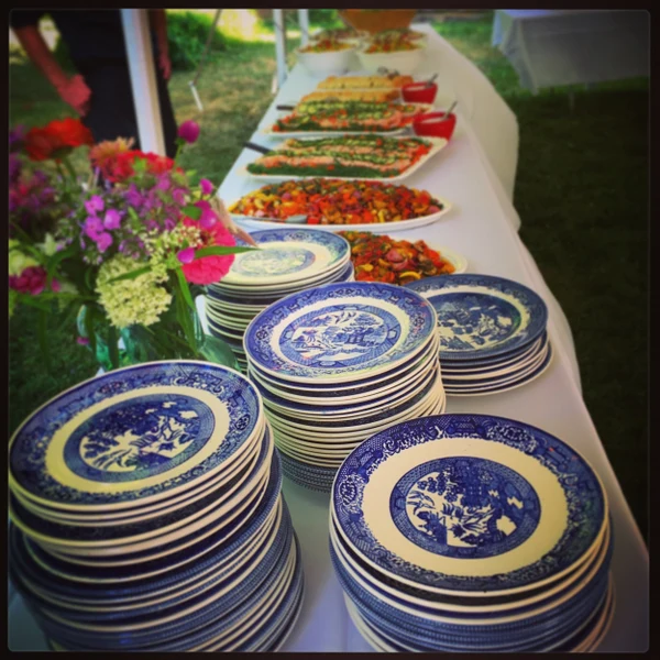 Word of Mouth Catering buffet under a tent with stacked blue and white plates and platters of salads