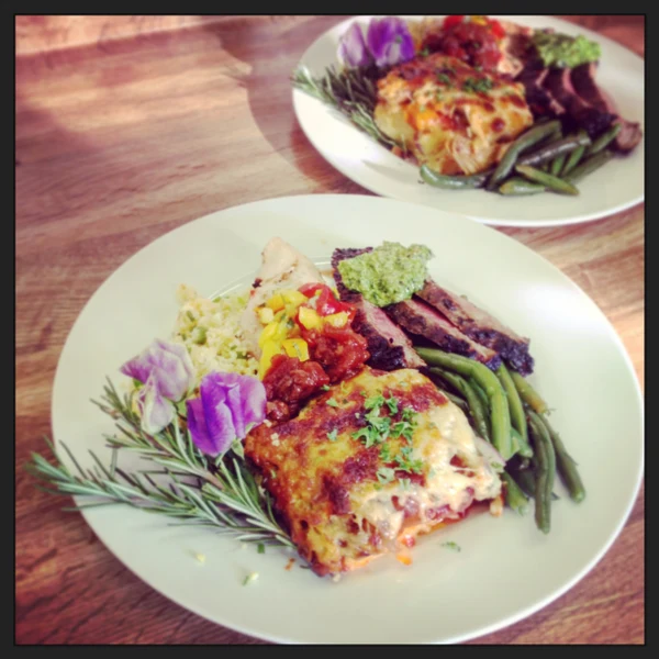 Word of Mouth Catering plated dinner with grilled meat, green beans and a baked gratin, garnished with rosemary and flowers