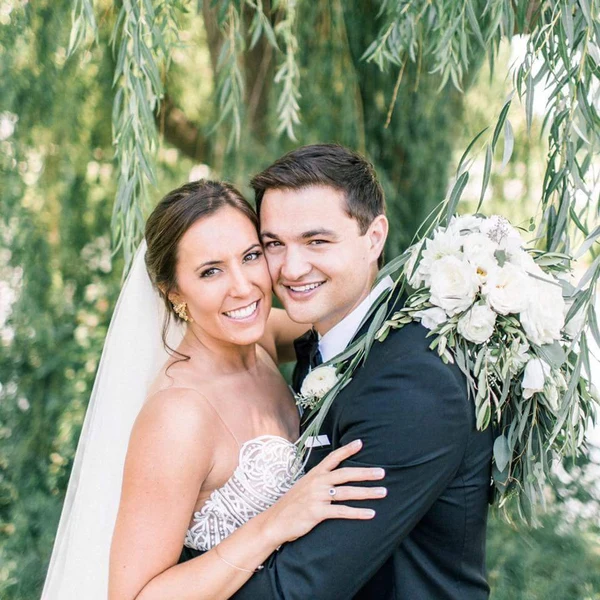 Northern Waves bride with soft makeup and swept-back hair beside the groom under trailing green branches