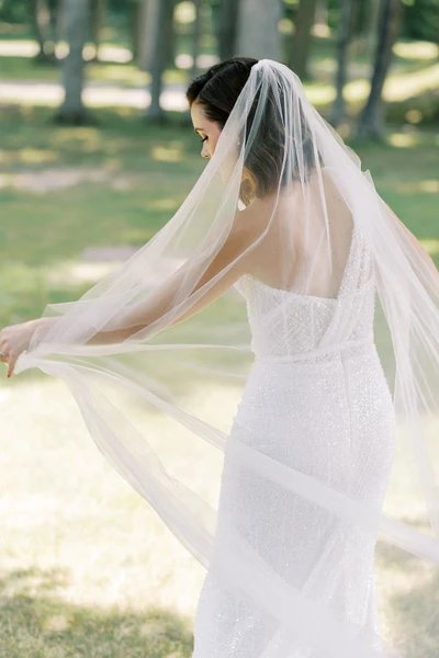 Northern Waves bride with dark hair under a long veil on a tree-lined lawn