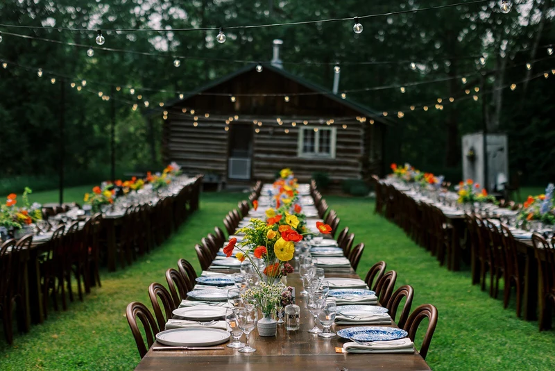 Fox & Fern Events outdoor wedding dinner with long tables and string lights in front of a log cabin