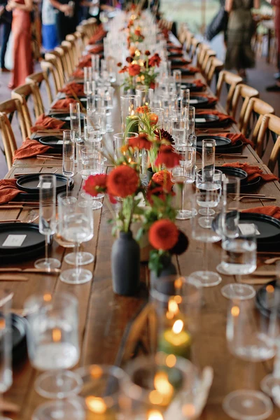 Fox & Fern Events long reception table with red and orange flowers, glassware and candles
